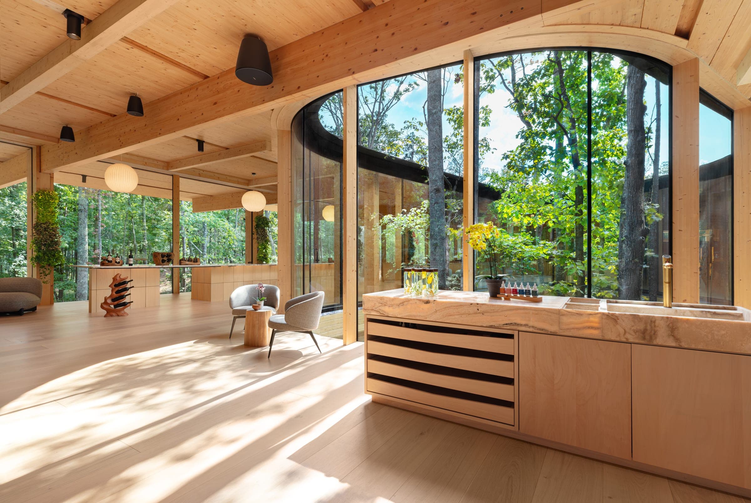 The bar and lounge at the courtyard glass — a stone counter with tasting bottles, two armchairs, trees in the glazed courtyard
