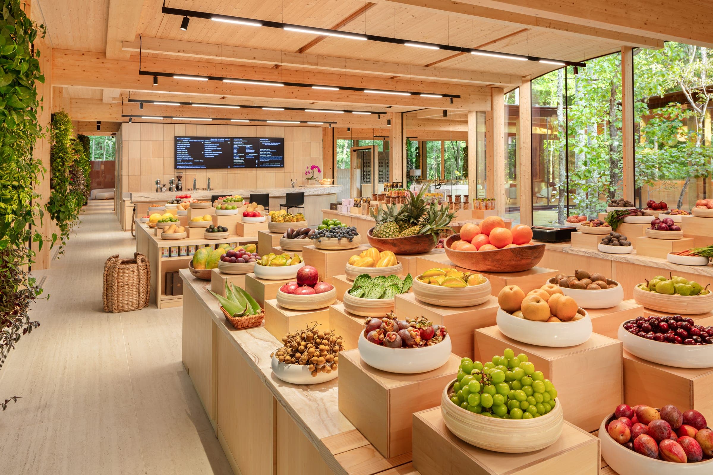 The Functional Market — fresh fruit in bowls and baskets on timber tables, the forest through the glass