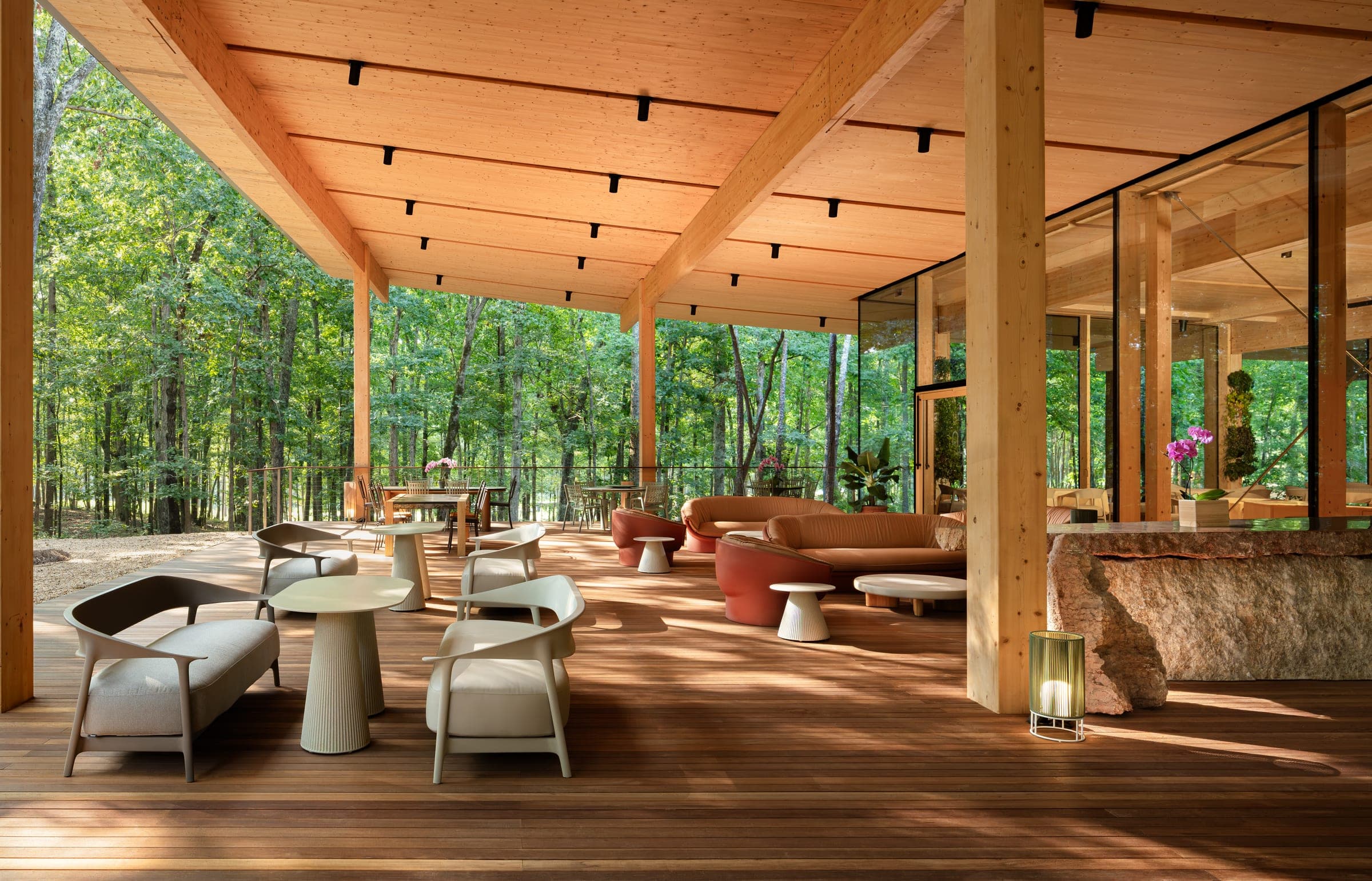 The Aviary pavilion — tables and lounge seating on the deck under the timber roof, forest on every side
