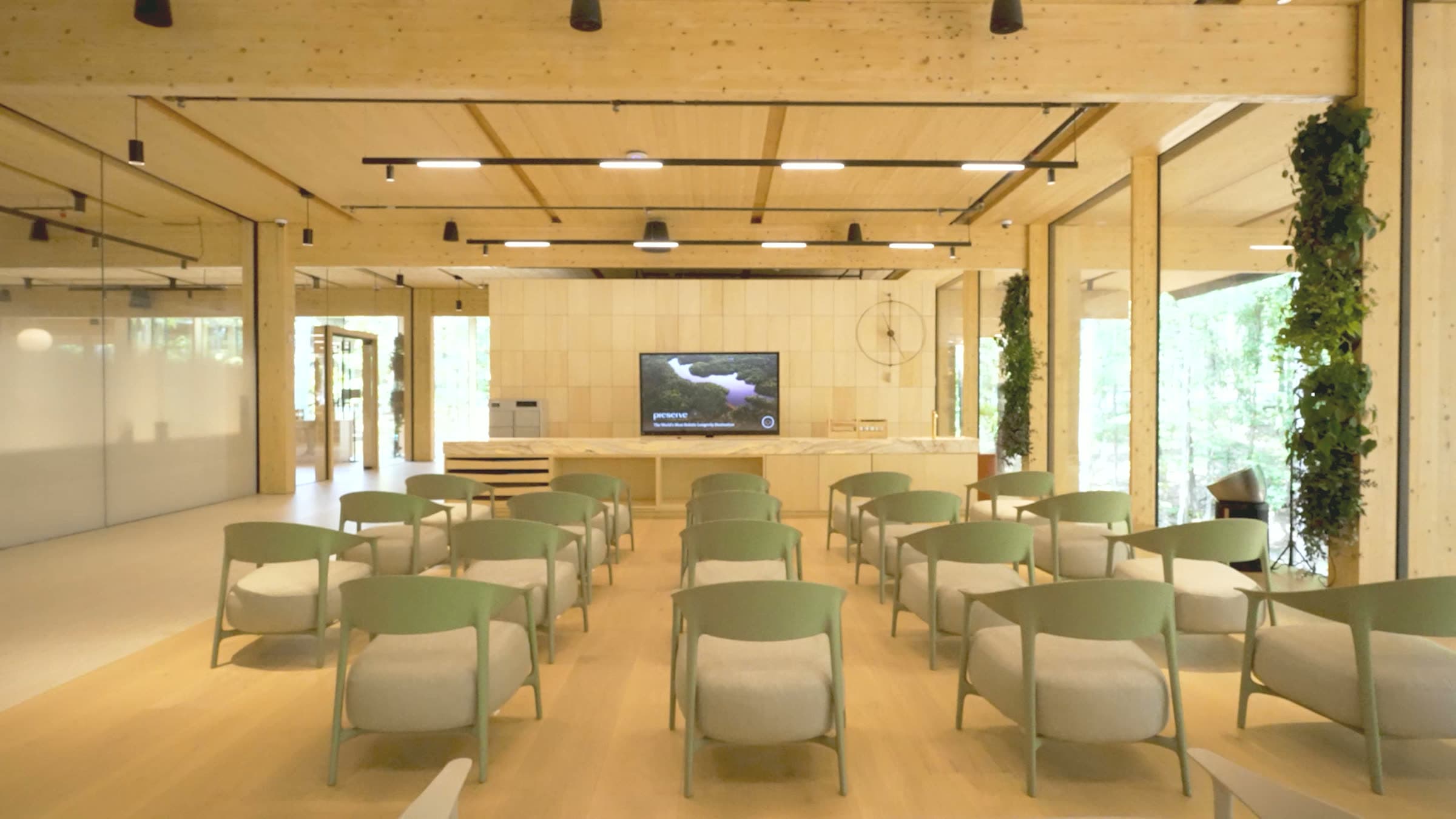 The Aviary set for a salon — rows of sage chairs facing the screen, the living wall and forest through the glass