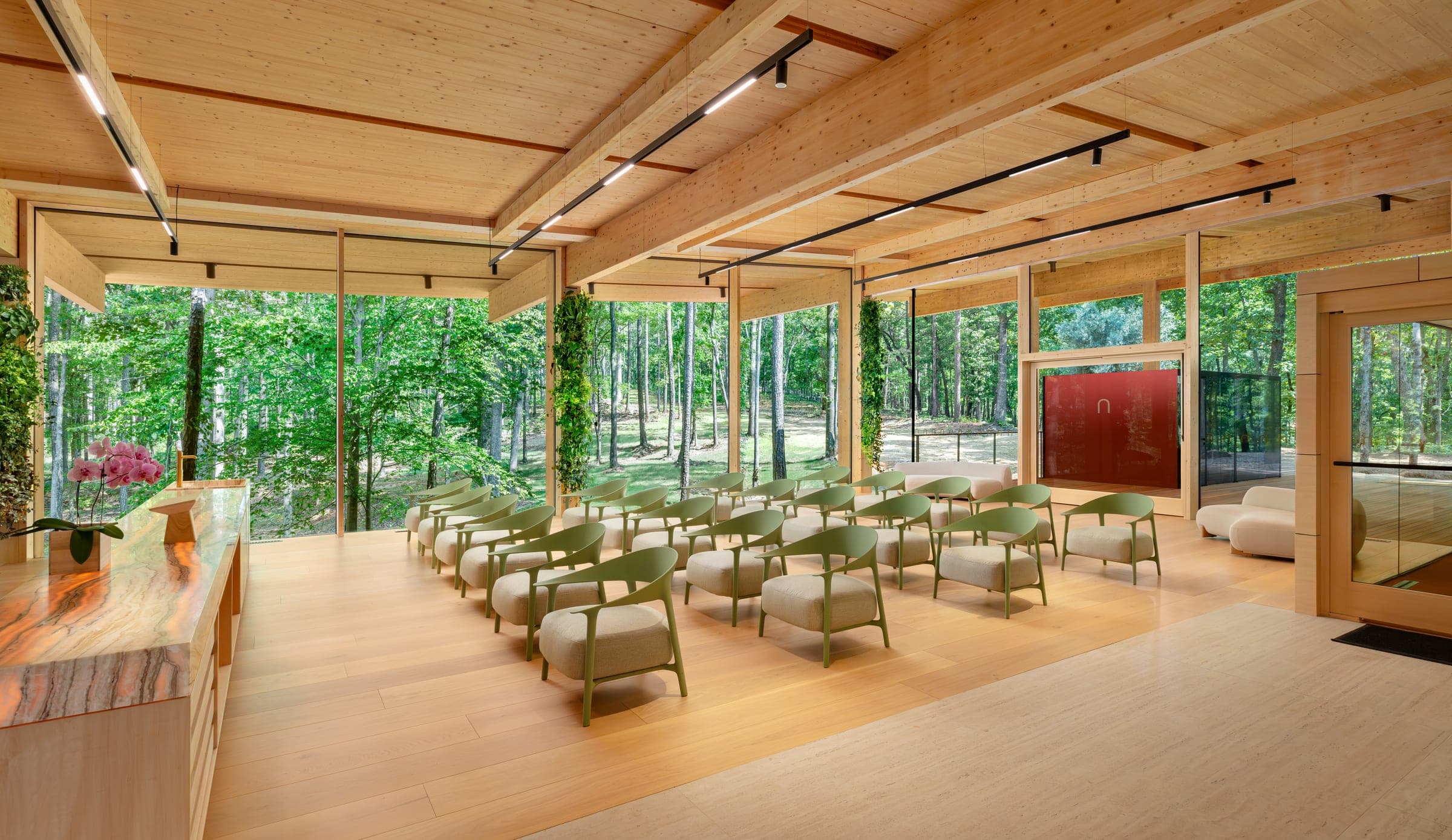 The Aviary — rows of sage chairs under the timber ceiling, glass walls onto the forest on every side